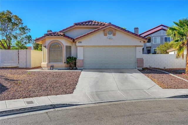 mediterranean / spanish-style home with a tiled roof, stucco siding, a garage, concrete driveway, and fence