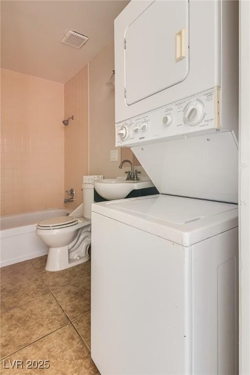 clothes washing area with stacked washer / drying machine and light tile patterned floors