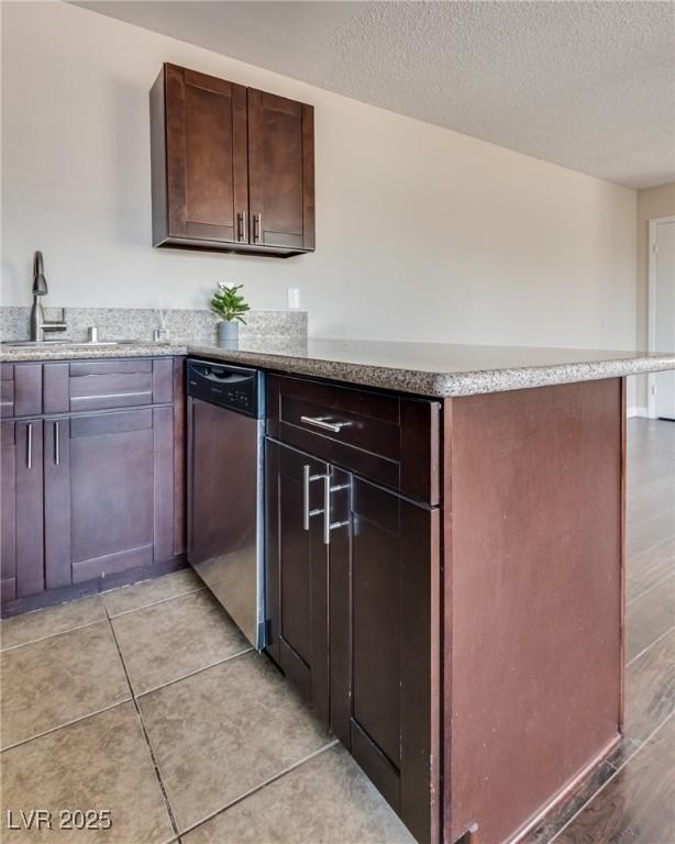 kitchen featuring stainless steel dishwasher, a sink, a peninsula, light stone counters, and a textured ceiling