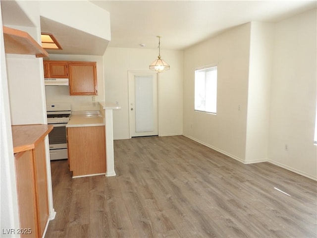 9470 Peace Way Unit 112, Las Vegas, NV 89147 - kitchen with white gas stove, light countertops, light wood-type flooring, under cabinet range hood, and pendant lighting