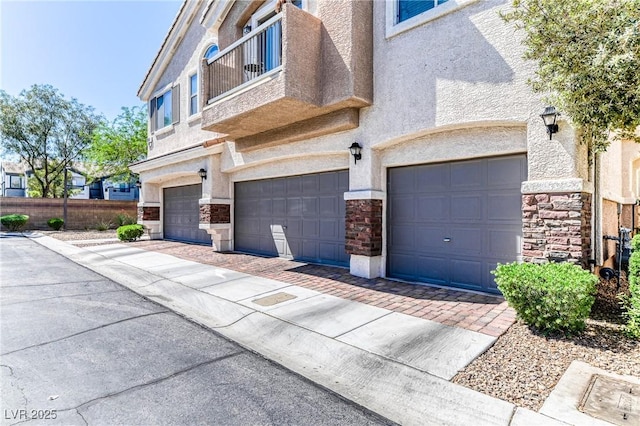 view of front of house featuring stone siding, a garage, stucco siding, driveway, and a balcony