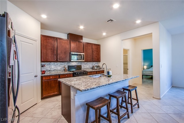 kitchen featuring freestanding refrigerator, stainless steel microwave, a sink, black range with gas stovetop, and light stone counters