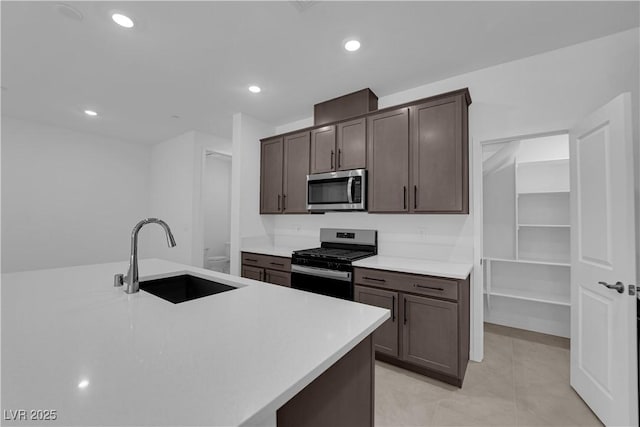 kitchen with appliances with stainless steel finishes, a sink, light countertops, dark brown cabinetry, and recessed lighting