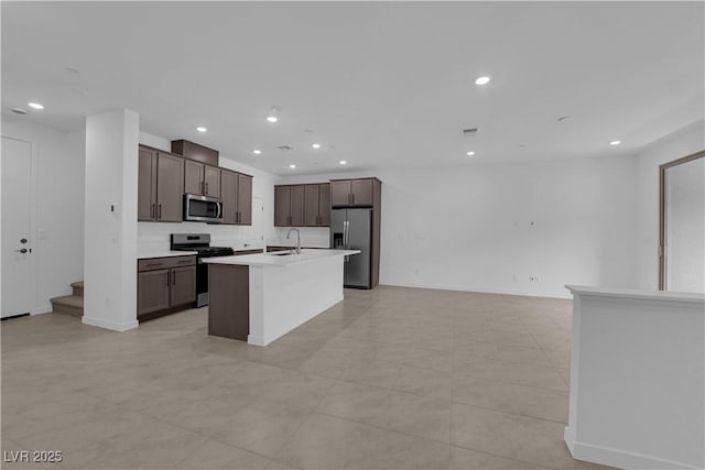 kitchen featuring stainless steel appliances, a sink, a center island with sink, open floor plan, and dark brown cabinetry