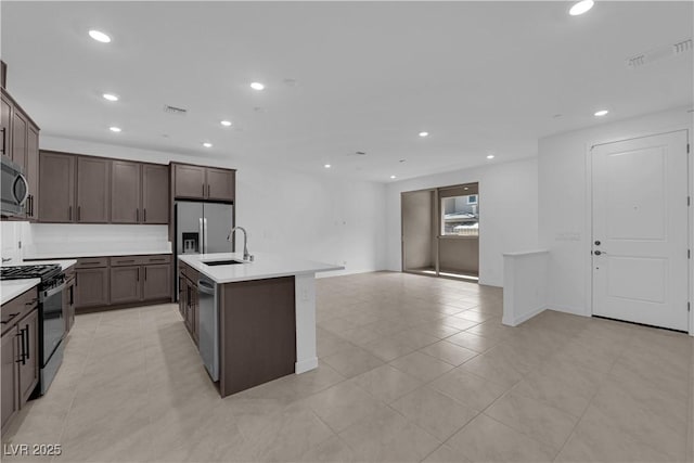kitchen featuring stainless steel appliances, a sink, dark brown cabinetry, light countertops, and a kitchen island with sink