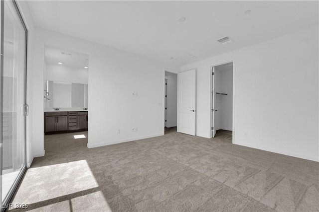 unfurnished bedroom featuring carpet floors, baseboards, ensuite bath, and a spacious closet