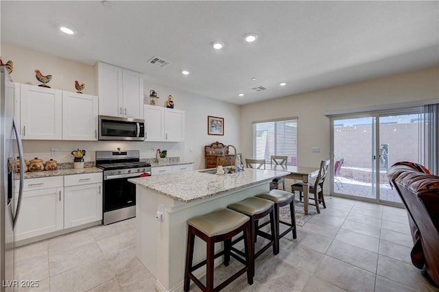387 Larksong Ave, Henderson, NV 89011 - kitchen with appliances with stainless steel finishes, a center island with sink, light stone counters, white cabinets, and a breakfast bar