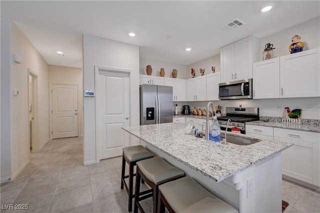 387 Larksong Ave, Henderson, NV 89011 - kitchen with stainless steel appliances, white cabinetry, an island with sink, a kitchen bar, and light stone countertops