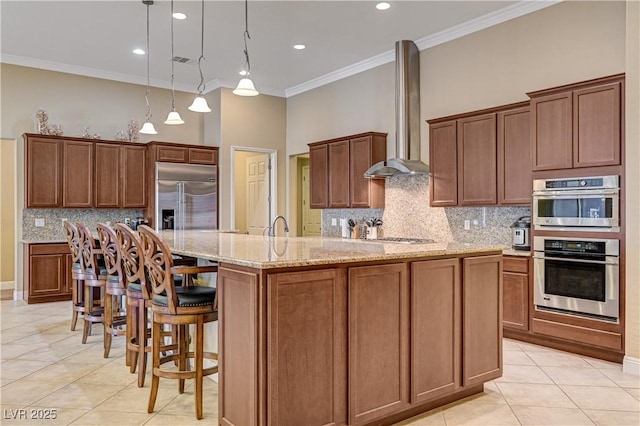 kitchen featuring appliances with stainless steel finishes, wall chimney range hood, light tile patterned flooring, crown molding, and a spacious island