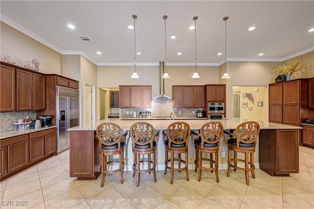 kitchen with stainless steel appliances, decorative backsplash, wall chimney exhaust hood, light tile patterned flooring, and a large island with sink