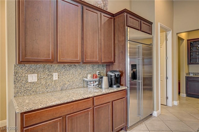 kitchen with built in fridge, light tile patterned floors, decorative backsplash, light stone counters, and baseboards