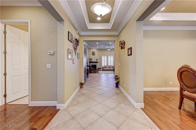 corridor with a tray ceiling, light wood-type flooring, ornamental molding, and baseboards