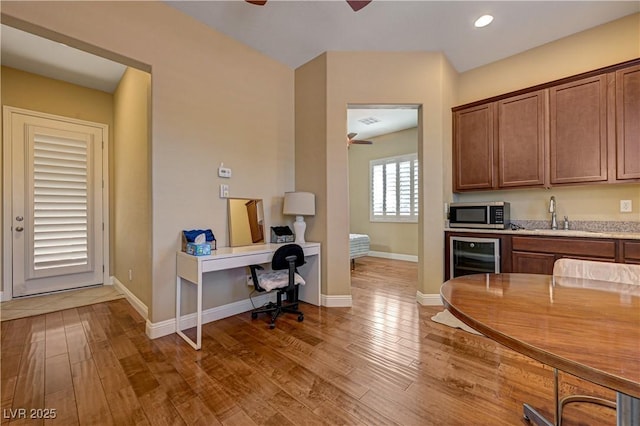 kitchen with ceiling fan, stainless steel microwave, a sink, wine cooler, and wood finished floors