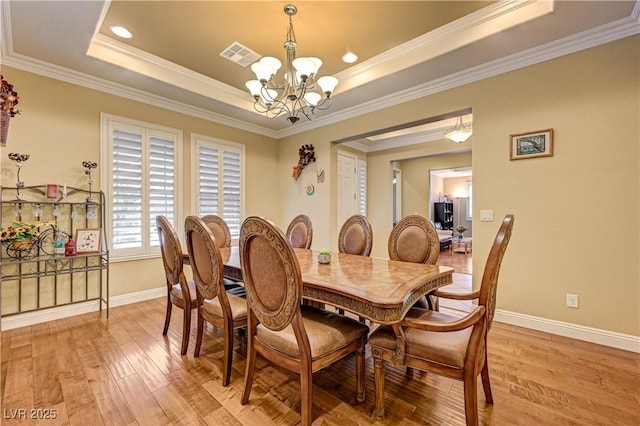 dining room with a chandelier, baseboards, light wood-style flooring, a tray ceiling, and crown molding