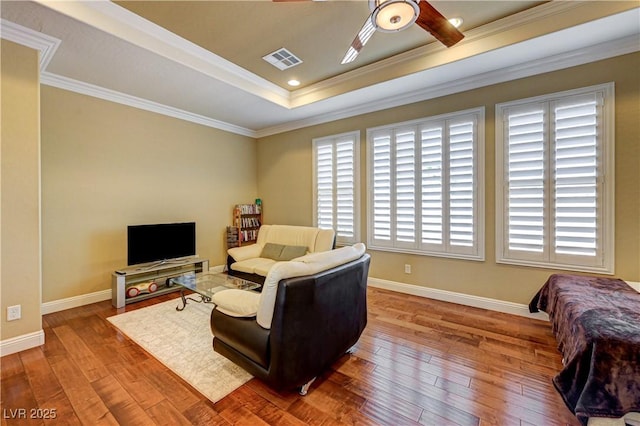 living room with ceiling fan, crown molding, hardwood / wood-style flooring, a raised ceiling, and baseboards