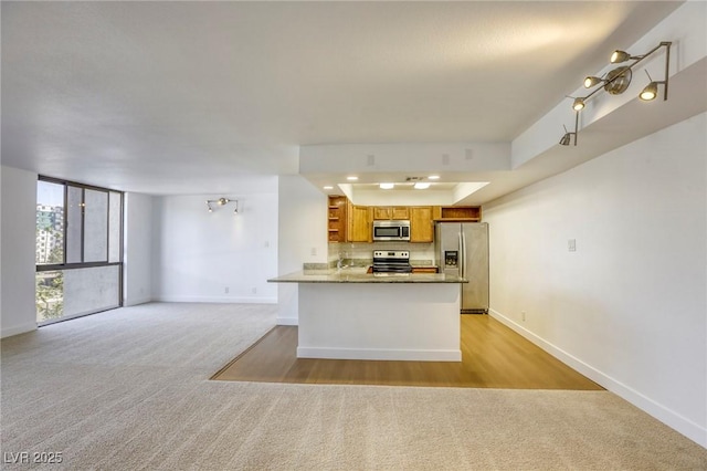 3930 University Center Dr Unit 311, Las Vegas, NV 89119 - kitchen with stainless steel appliances, light carpet, baseboards, brown cabinetry, and a peninsula