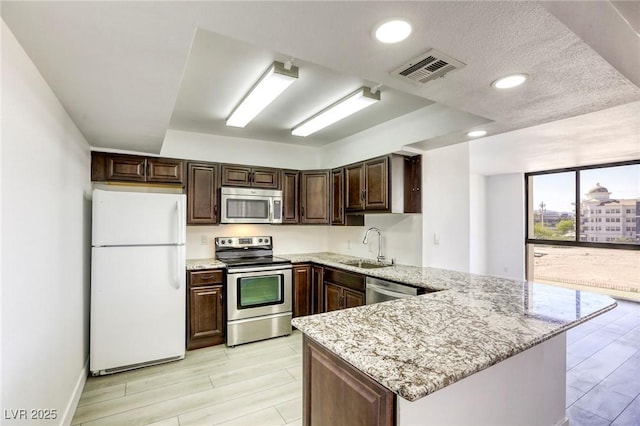 3930 University Center Dr Unit 312, Las Vegas, NV 89119 - kitchen featuring stainless steel appliances, a peninsula, a sink, dark brown cabinetry, and light stone countertops