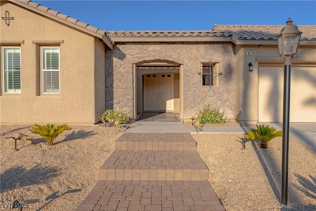 8228 Fulton Ranch St, Las Vegas, NV 89131 - entrance to property featuring stone siding, an attached garage, a tile roof, and stucco siding