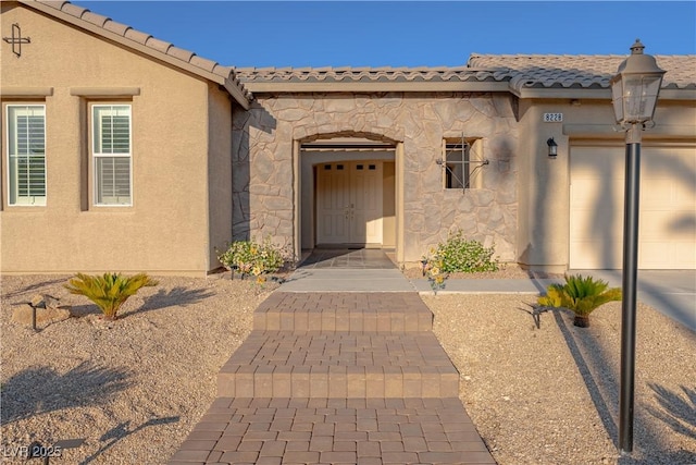 entrance to property with stone siding, a garage, a tiled roof, and stucco siding