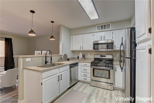 kitchen featuring stainless steel appliances, a sink, light wood-style flooring, and a peninsula