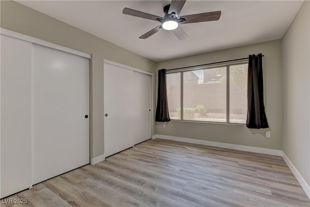 unfurnished bedroom with multiple closets, light wood-style flooring, baseboards, and ceiling fan