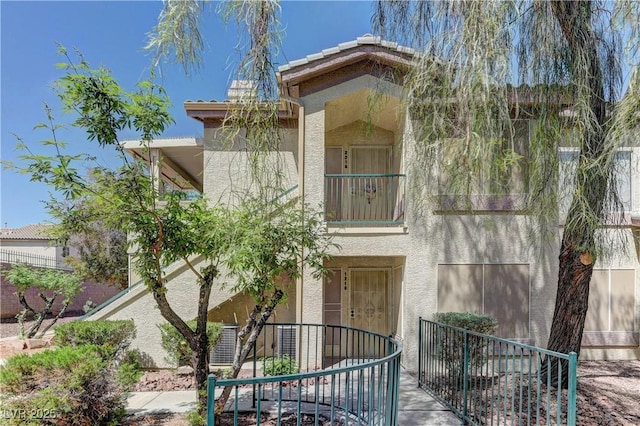 view of front of property with stucco siding, a balcony, and fence