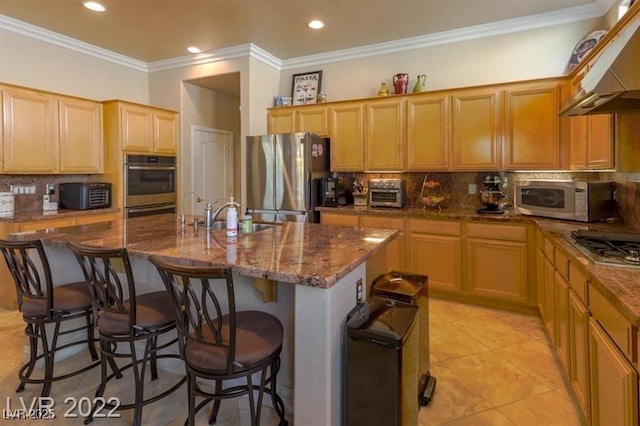 kitchen with appliances with stainless steel finishes, under cabinet range hood, tasteful backsplash, a center island with sink, and a kitchen breakfast bar