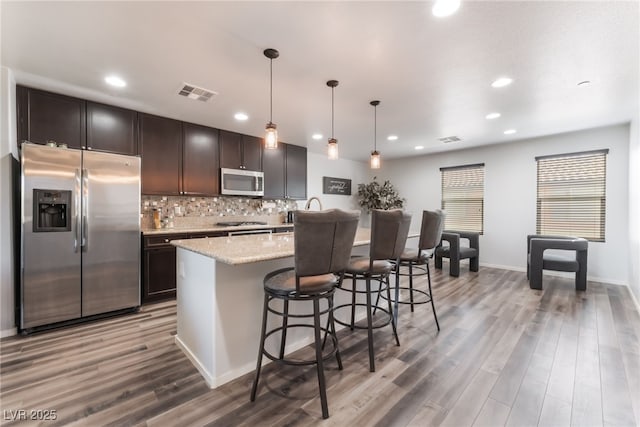 4650 Ranch House Rd Unit 86, North Las Vegas, NV 89031 - kitchen with stainless steel appliances, wood finished floors, dark brown cabinetry, a center island with sink, and backsplash