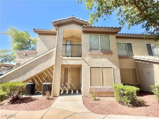 rear view of house featuring stucco siding, central AC, a balcony, and a tiled roof