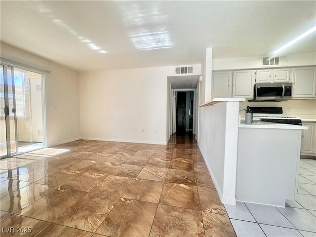 kitchen featuring stainless steel microwave, range, light countertops, light marble finish floors, and baseboards