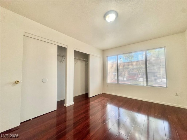 unfurnished bedroom with wood finished floors, multiple closets, and baseboards