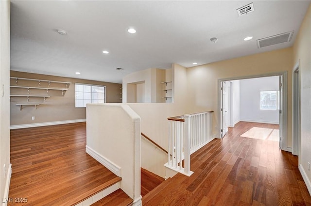 hallway with an upstairs landing, wood finished floors, baseboards, and recessed lighting