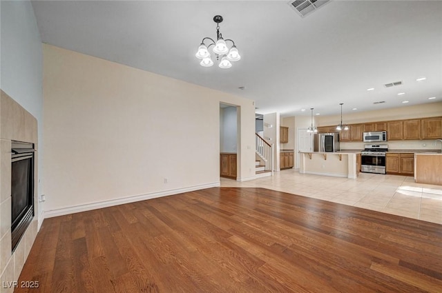 unfurnished living room featuring a chandelier, light wood finished floors, stairs, a glass covered fireplace, and recessed lighting