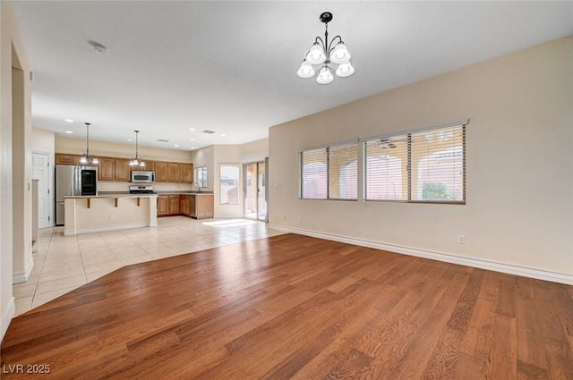 unfurnished living room with a chandelier, baseboards, light wood-type flooring, and recessed lighting