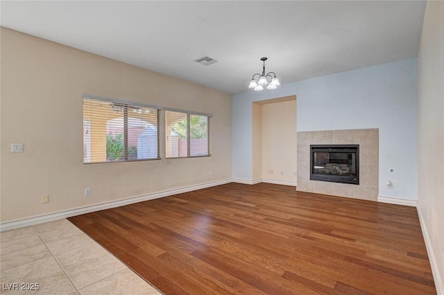 unfurnished living room with a chandelier, wood finished floors, a tile fireplace, and baseboards