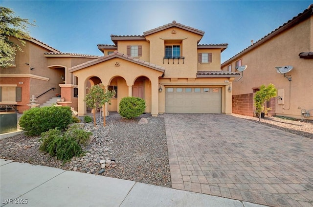 mediterranean / spanish-style house with a garage, a tile roof, stucco siding, and decorative driveway