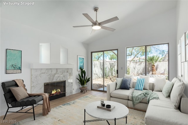 living room with light wood-style floors, a premium fireplace, a ceiling fan, and high vaulted ceiling