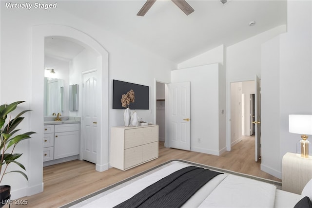 bedroom with light wood finished floors, a sink, baseboards, high vaulted ceiling, and ensuite bath