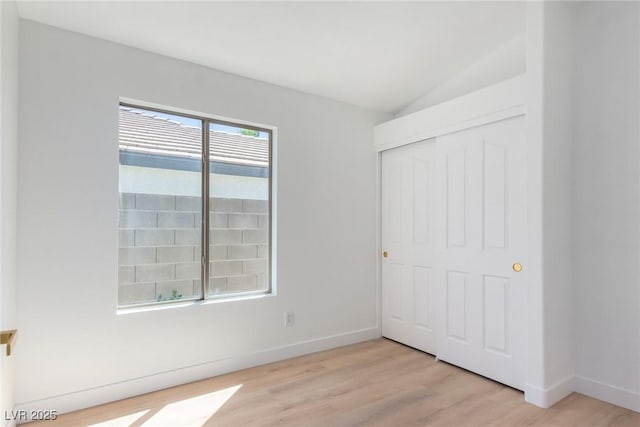 unfurnished bedroom with light wood-type flooring, lofted ceiling, a closet, and baseboards