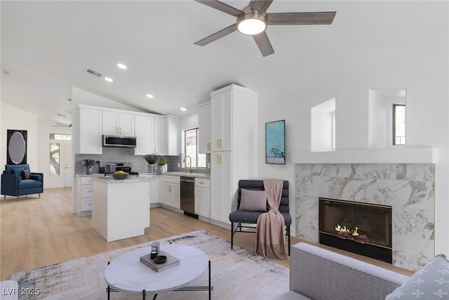 living room featuring ceiling fan, vaulted ceiling, light wood-style floors, a fireplace, and recessed lighting