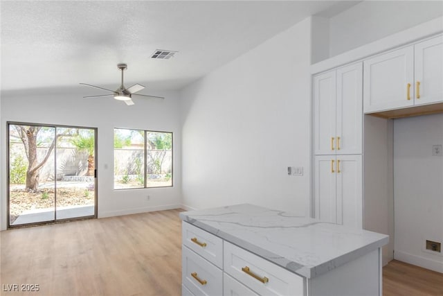 kitchen featuring light wood finished floors, white cabinetry, a ceiling fan, light stone counters, and a center island