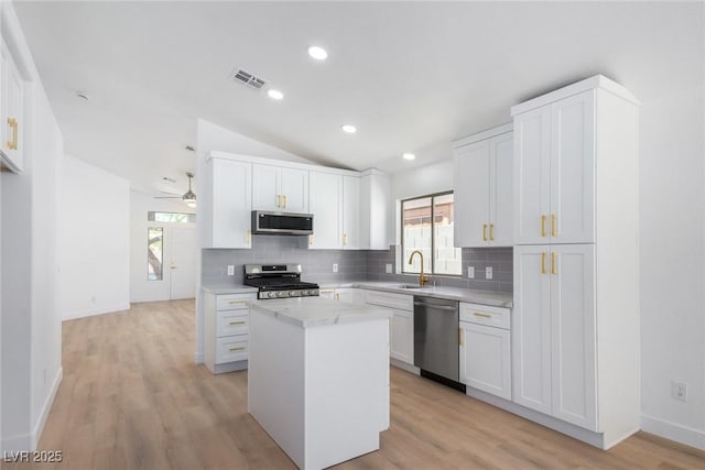 kitchen with stainless steel appliances, tasteful backsplash, a sink, light countertops, and vaulted ceiling