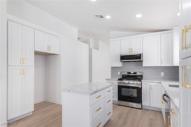 kitchen featuring stainless steel appliances, light wood finished floors, decorative backsplash, a center island, and light stone countertops