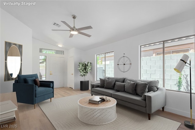 living area with a ceiling fan, light wood-type flooring, vaulted ceiling, and baseboards