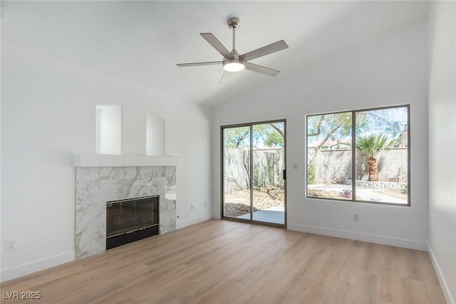 unfurnished living room with a high end fireplace, high vaulted ceiling, light wood-type flooring, ceiling fan, and baseboards