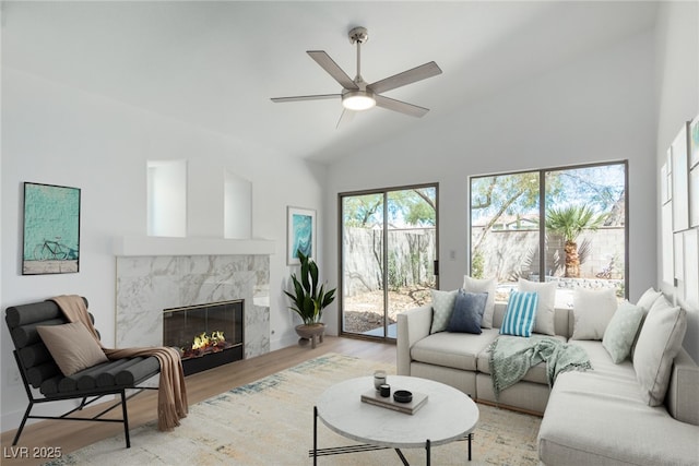 living room with light wood finished floors, a high end fireplace, ceiling fan, and high vaulted ceiling