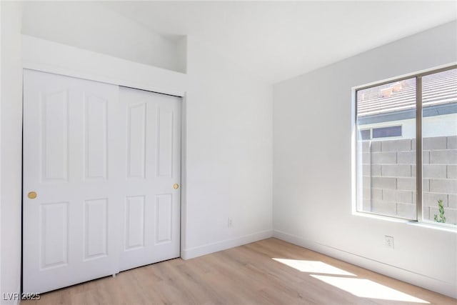 unfurnished bedroom featuring wood finished floors, multiple windows, a closet, baseboards, and vaulted ceiling