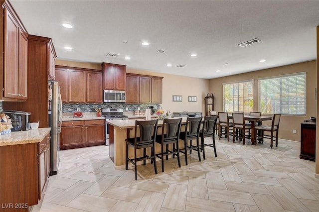 kitchen featuring stainless steel appliances, a center island with sink, a breakfast bar area, decorative backsplash, and recessed lighting