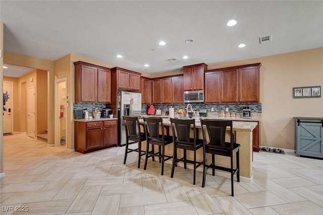 kitchen with appliances with stainless steel finishes, backsplash, a kitchen breakfast bar, a center island with sink, and baseboards