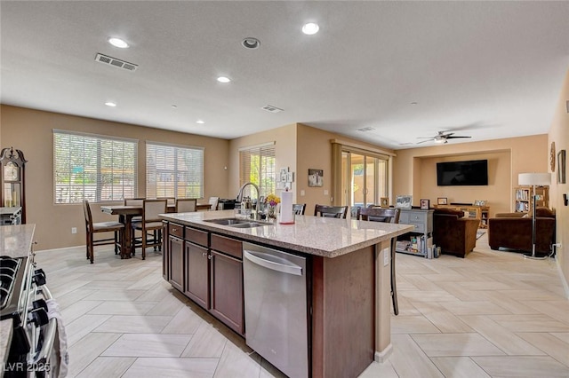 kitchen featuring appliances with stainless steel finishes, a sink, light stone countertops, a kitchen island with sink, and recessed lighting